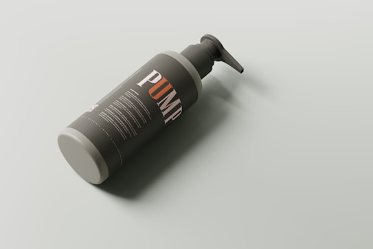 A bottle with a pump dispenser is lying on its side against a light-colored background. The bottle is dark with some text, including the large word 'PUMP' in contrasting white and orange colors.