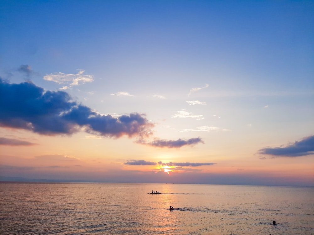 the sun is setting over the ocean with boats in the water