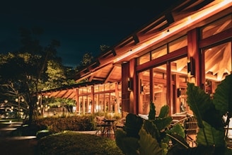 A cozy post and beam tasting room glowing warmly at sunset, surrounded by lush greenery.