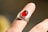 A silver ring featuring a large, oval red gemstone is worn on an adult's finger. The background is blurred, highlighting the intricacy of the ring's design and the vividness of the gemstone.
