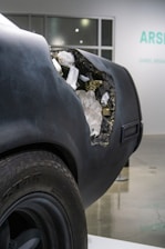The rear of a matte black car reveals an artistic detail where the body appears to be eroded, exposing a cluster of crystals and minerals inside. This contrast between the rough exterior and the delicate, shimmering interior creates an intriguing visual impact.