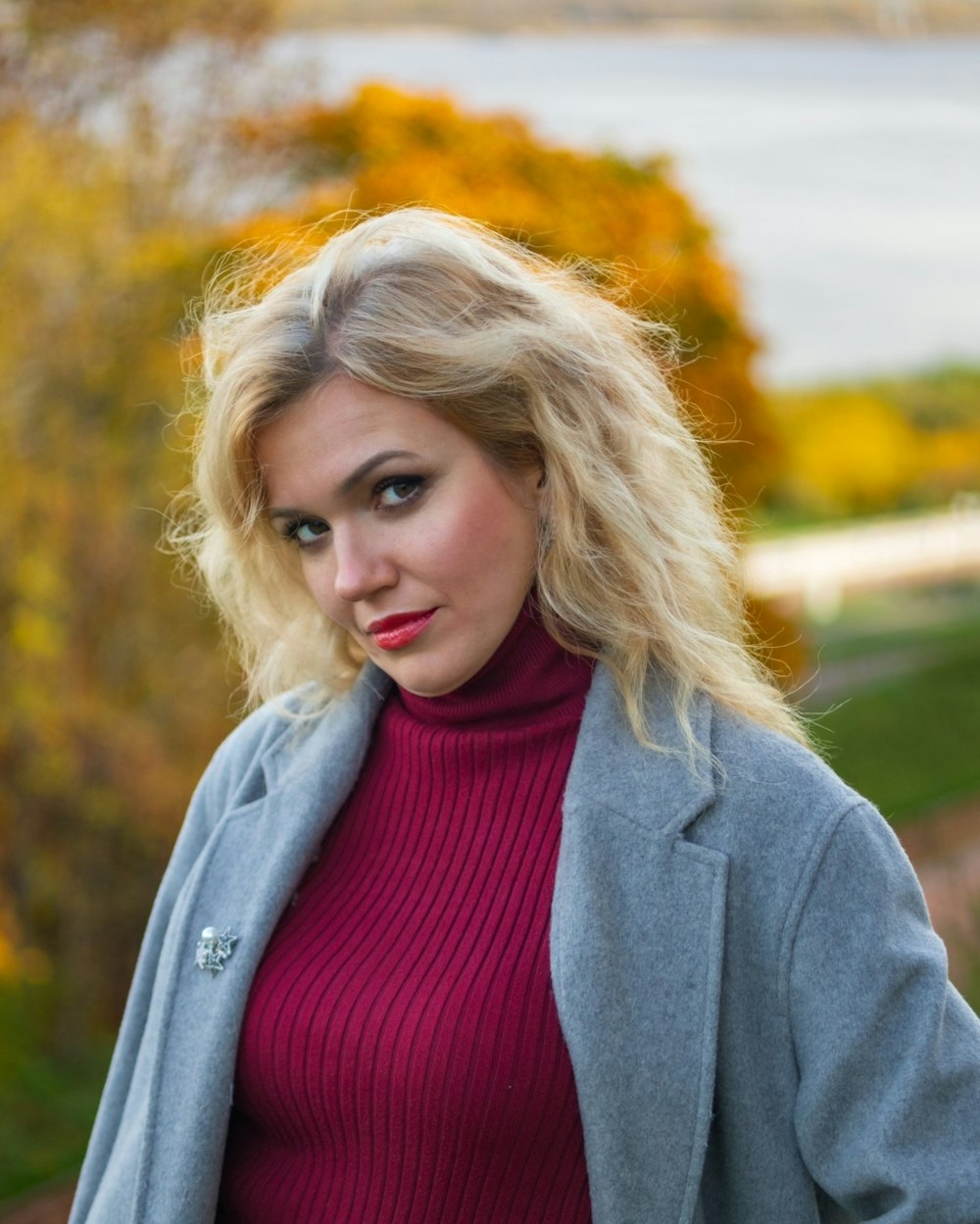 a woman with blonde hair wearing a red sweater and a gray coat