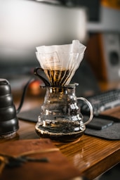 a glass coffee pot filled with liquid on top of a wooden table