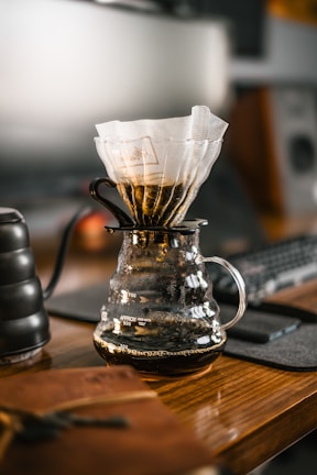 a glass coffee pot filled with liquid on top of a wooden table