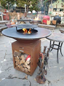 A clean and ready-to-use fire pit with accessories neatly arranged on a patio.