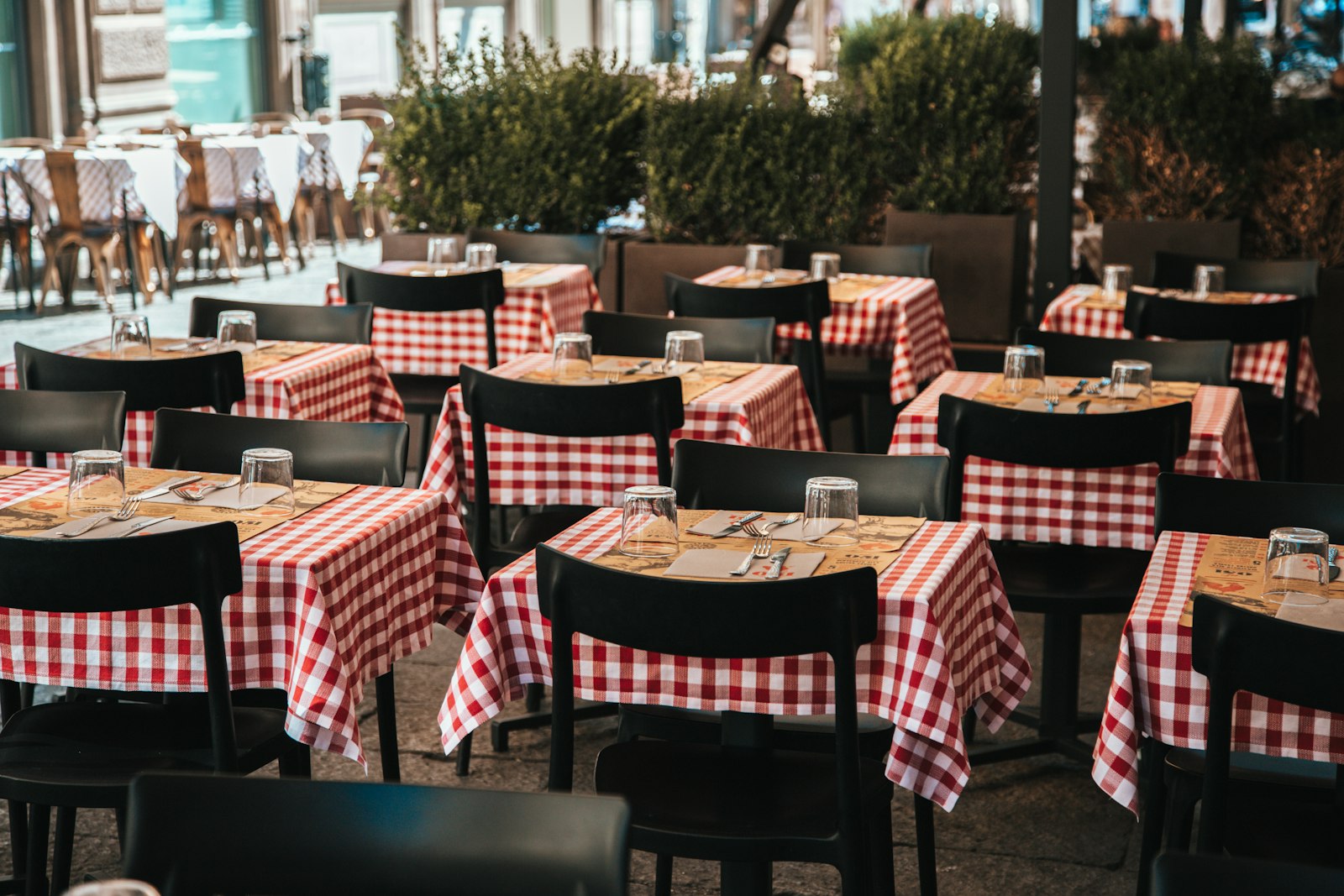Rows of trattoria tables with red-and-white checked tablecloths set for a meal in Bologna