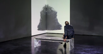 Visitors seated on minimalist benches, deeply absorbed in a multimedia queer art exhibit projected on the gallery wall.