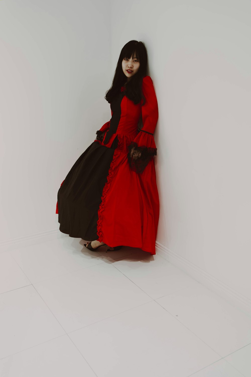 a woman in a red and black dress leaning against a wall