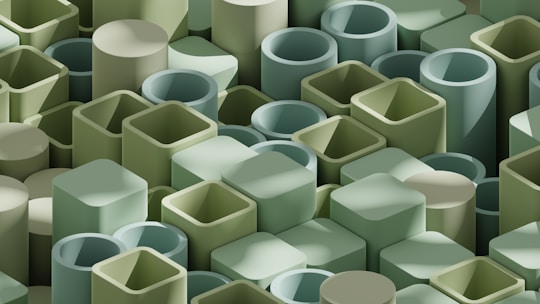 An array of 3D geometric shapes, including cylinders and rectangular prisms, arranged in a dense pattern. The shapes are predominantly in shades of green, creating a harmonious and uniform visual appearance.