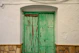 a green door with a white wall and stone floor
