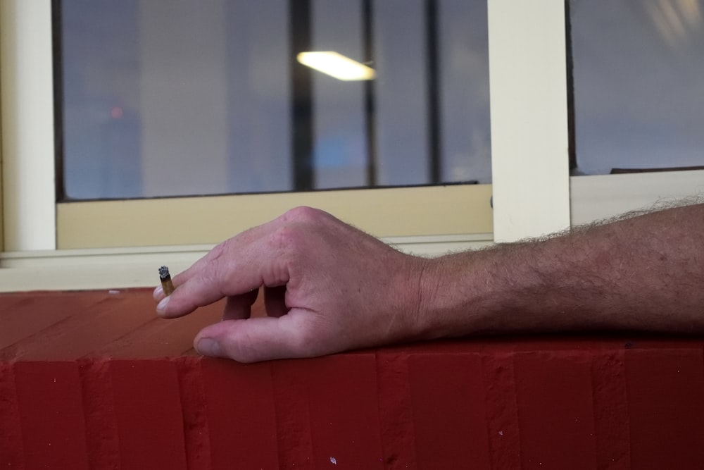 a man's hand holding a cigarette in front of a window