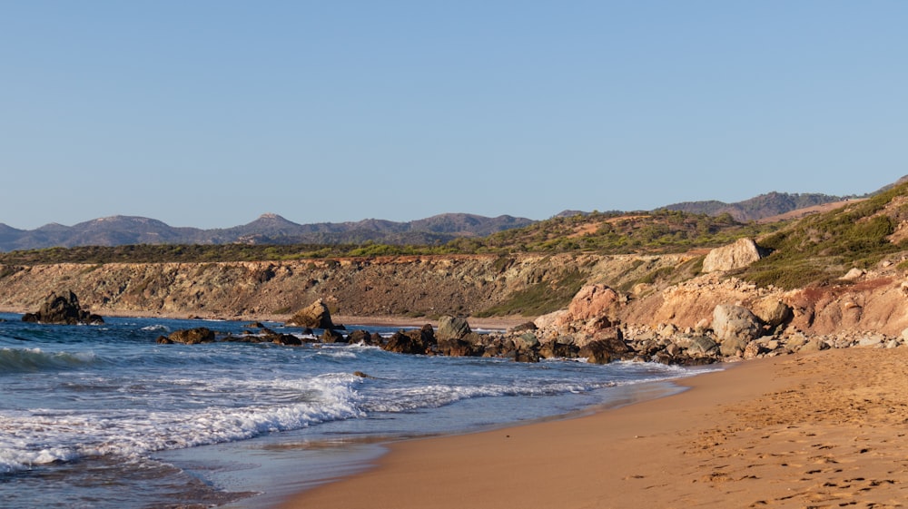 a sandy beach next to the ocean with mountains in the background