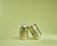 Two metallic cans with branding are positioned against a light green background. One can is slightly tilted and leaning against the other.