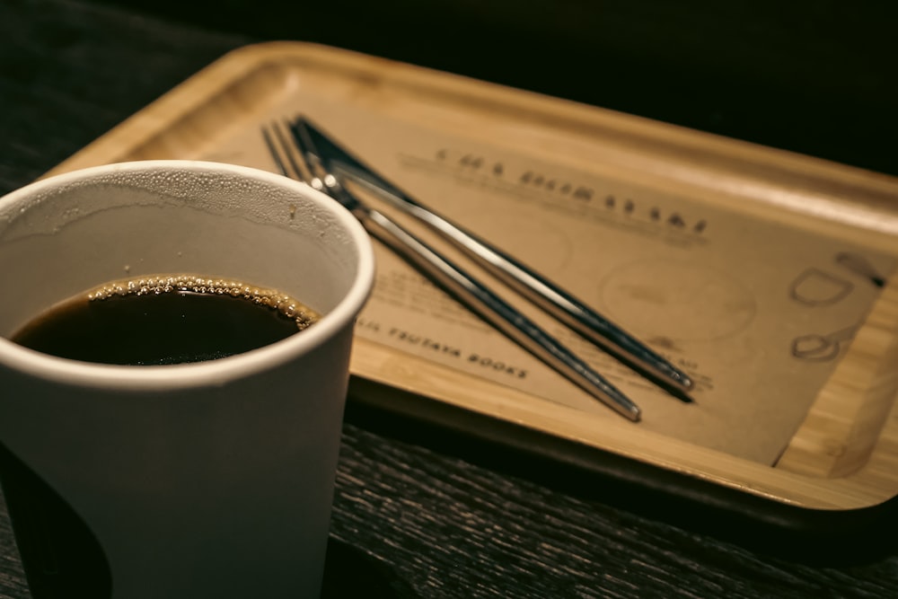 a cup of coffee next to a tray with chopsticks