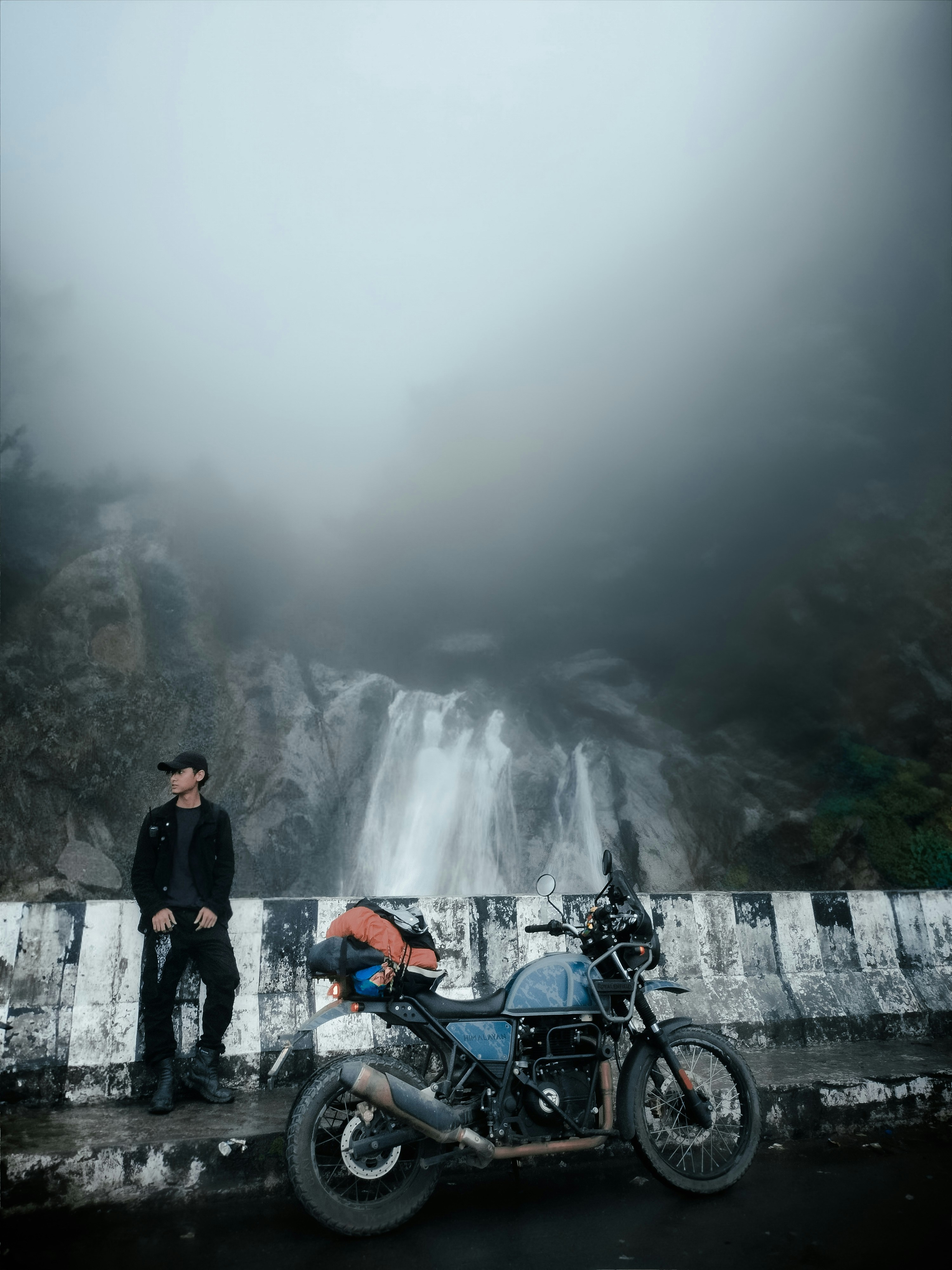 Seorang pria berdiri di samping sepeda motor di dekat air terjun
