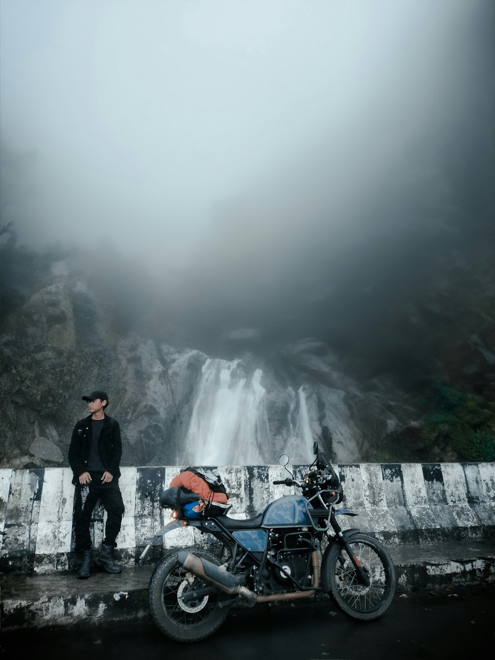 a man standing next to a motorcycle near a waterfall