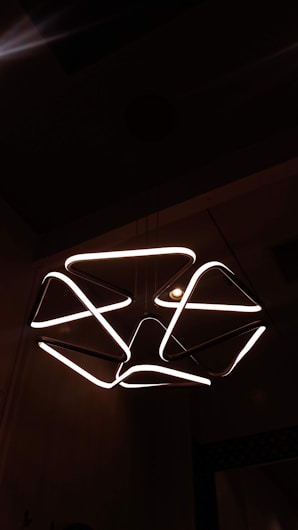 A modern chandelier with geometric shapes emitting a warm white light, creating an artistic and contemporary look against a dark background.