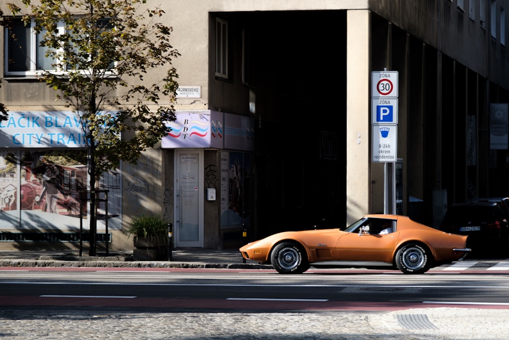 an orange car driving down a street next to a tall building