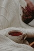 A cozy scene showing a tea cup shaped as a thoughtful face, surrounded by loose tea leaves and a teapot.