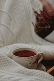 Soft cream-colored blanket folded next to a steaming cup of tea on a wooden table.