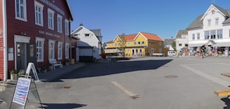 A bright, sunny street scene showing a single-story commercial building and a cozy house with gleaming windows.