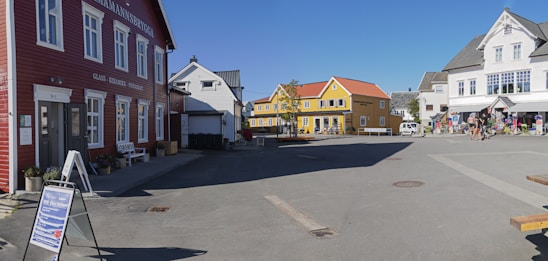 A bright, sunny street scene showing a single-story commercial building and a cozy house with gleaming windows.