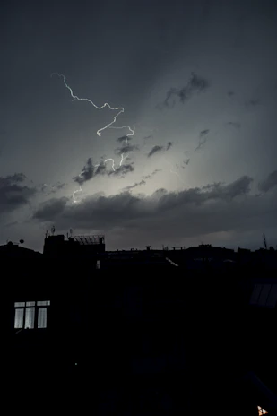 A cinematic shot of a city skyline at dusk with lightning subtly illuminating the clouds.