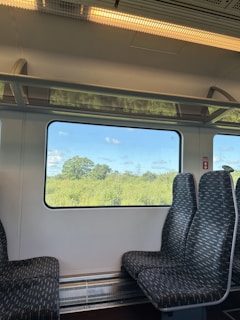 Close-up of a comfortable train seat with a window view of green fields and blue skies.