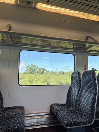 Close-up of a comfortable train seat with a window view of green fields and blue skies.