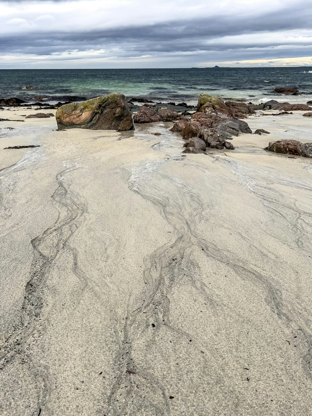 a sandy beach with rocks and water in the background