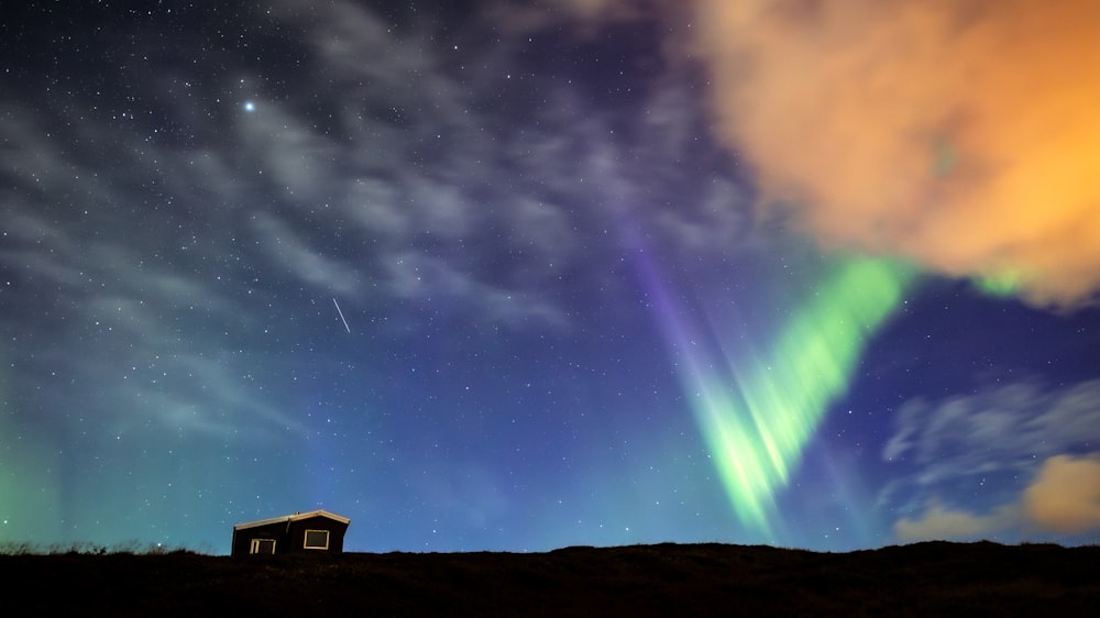 a house sitting on top of a hill under a sky filled with stars