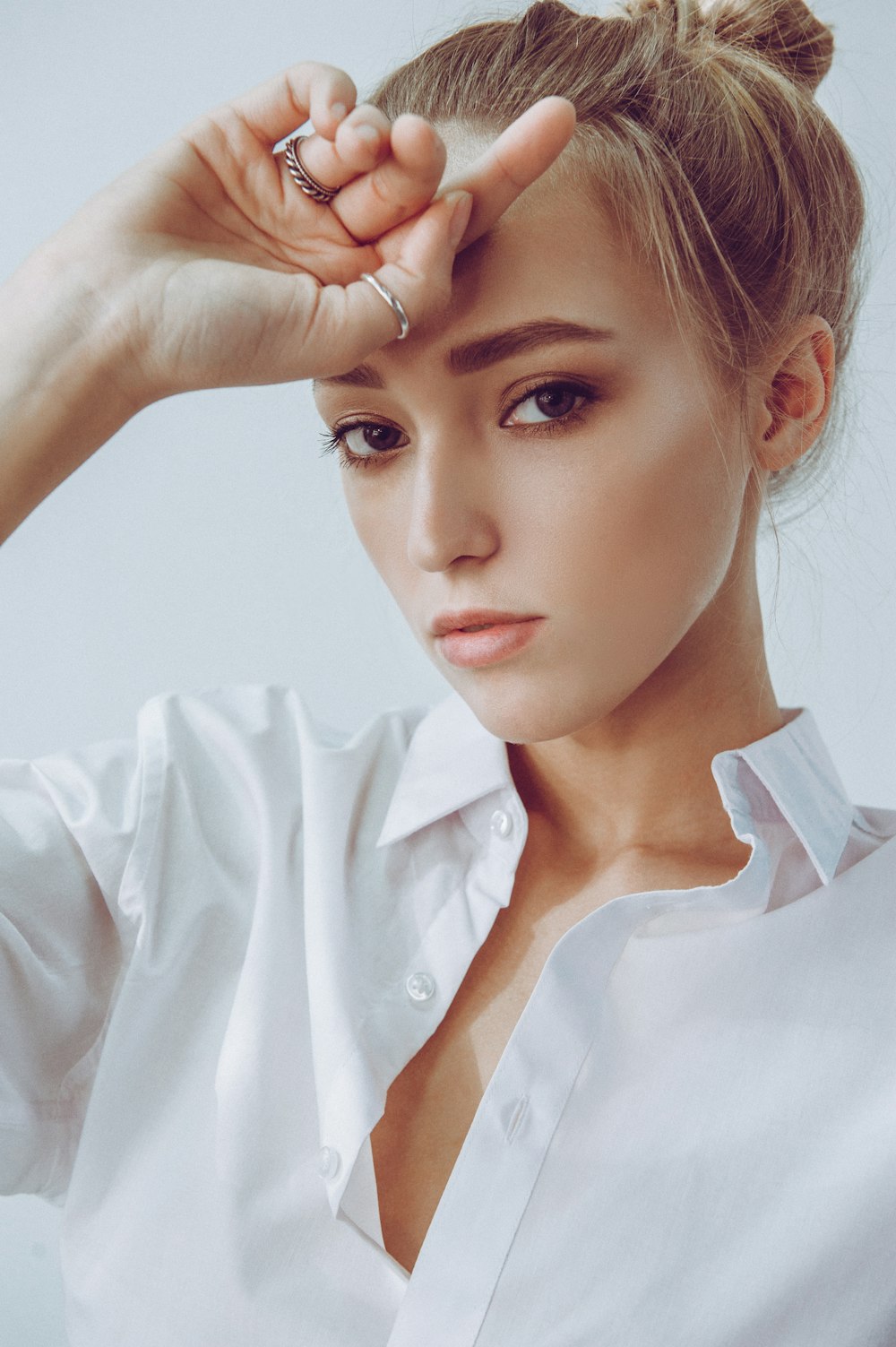 a woman in a white shirt is holding her hand up to her head