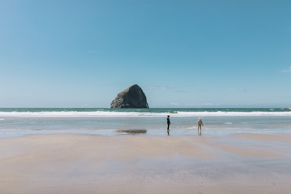 two people standing on a beach next to the ocean