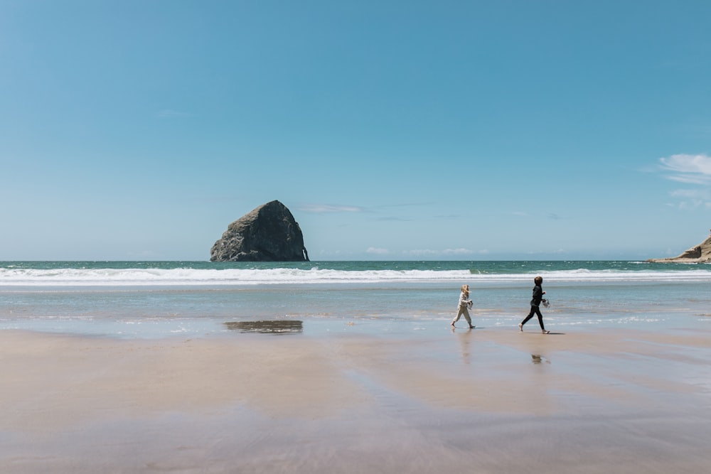 a couple of people walking across a sandy beach