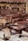 A traditional tannery with multiple circular vats filled with different colored liquids, surrounded by an old building with drying hides hanging along the walls. Workers are seen tending to the vats and processing hides using long sticks and tools.