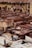 A traditional tannery with multiple circular vats filled with different colored liquids, surrounded by an old building with drying hides hanging along the walls. Workers are seen tending to the vats and processing hides using long sticks and tools.