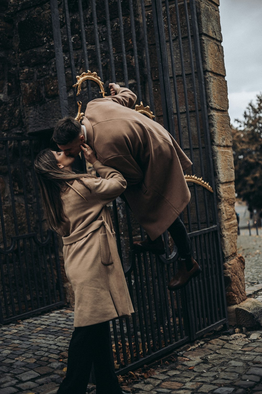 a man and a woman kissing in front of a gate