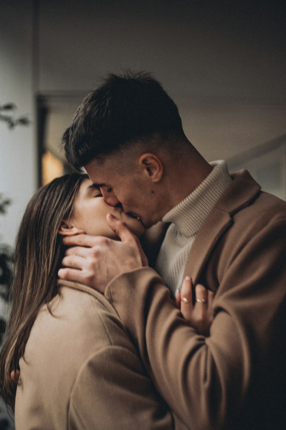 a man and a woman kissing in front of a plant