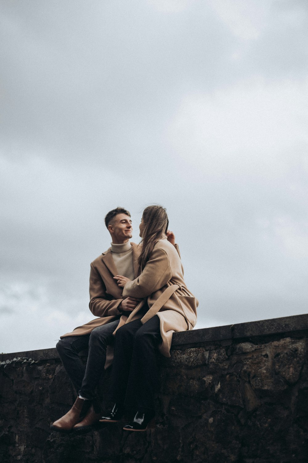 a man and a woman sitting on a stone wall