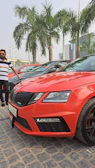 Bright red Swift hatchback parked by a sunny Goan beachside road.