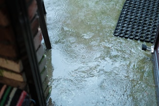 A sturdy, textured non-slip outdoor doormat on a rainy patio catching dirt and moisture.