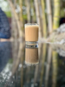 A glass of fresh, creamy soya milk with a subtle peacock feather pattern in the background.