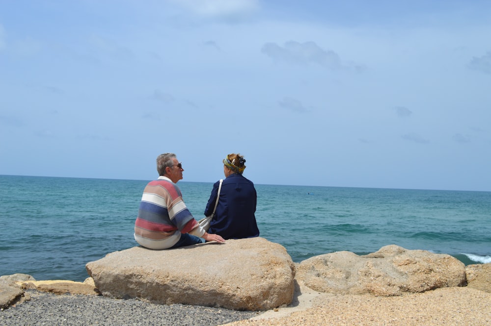 a couple of people sitting on top of a rock near the ocean