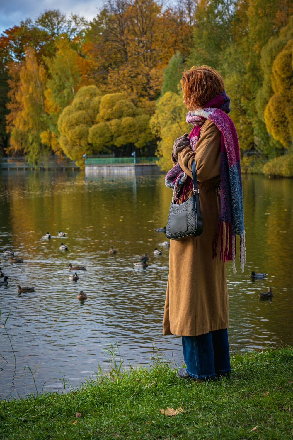 a woman is standing by a pond with ducks