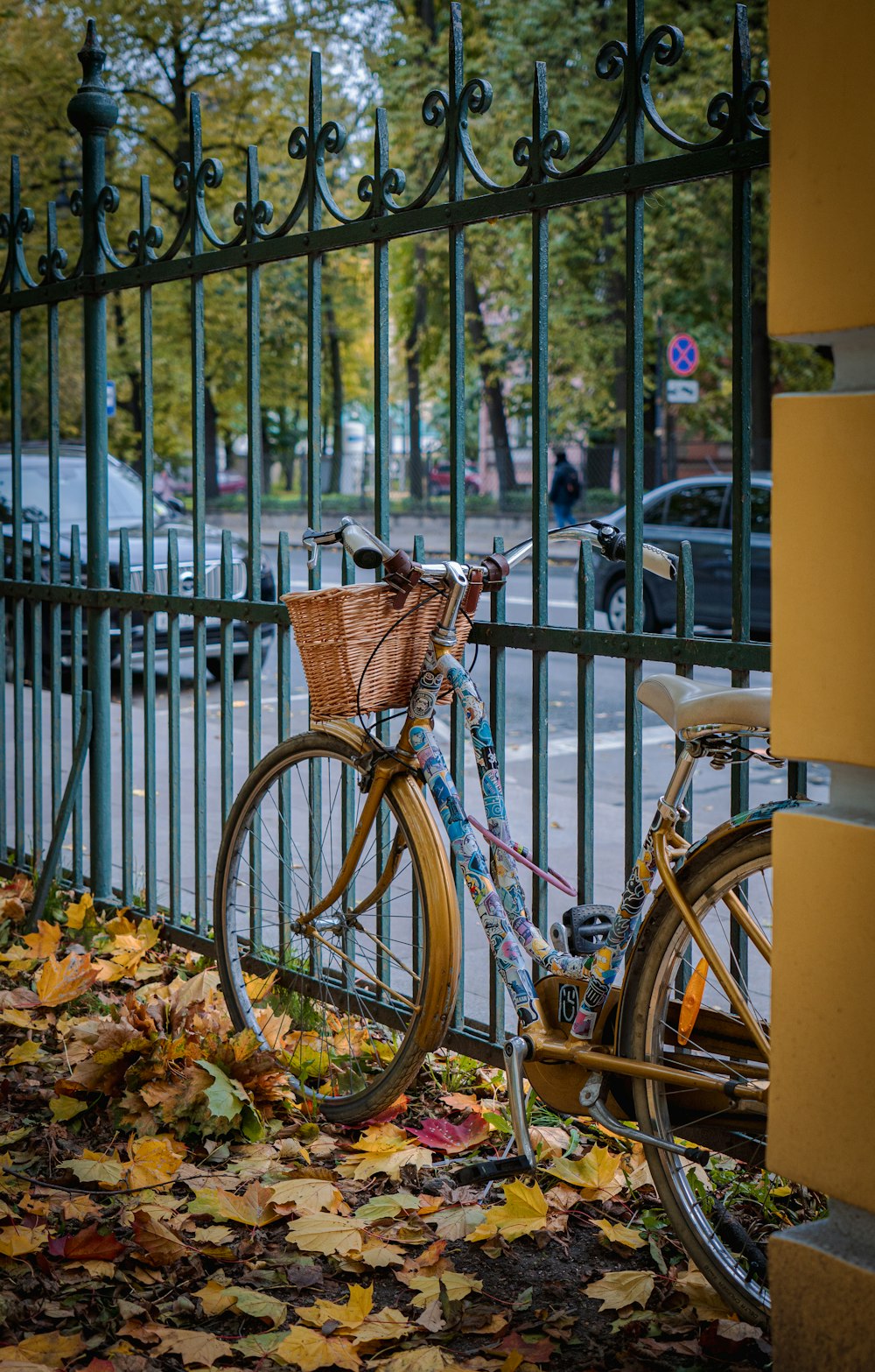 a bicycle parked next to a fence with autumn leaves on the ground