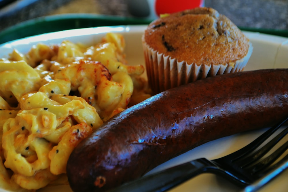 a sausage, macaroni and cheese and a muffin on a plate