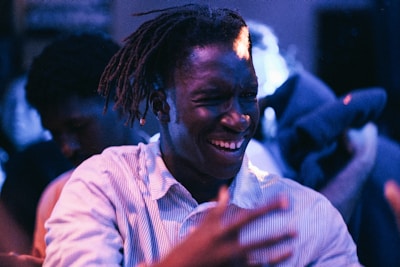 A person wearing a striped shirt is captured in a moment of joy, possibly dancing or celebrating, with vibrant lighting and a blurred background that seems to be in a party or club setting. Their expression suggests happiness and energy.