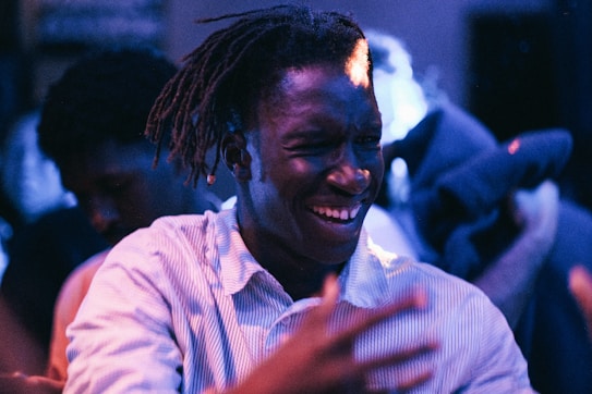 A person wearing a striped shirt is captured in a moment of joy, possibly dancing or celebrating, with vibrant lighting and a blurred background that seems to be in a party or club setting. Their expression suggests happiness and energy.