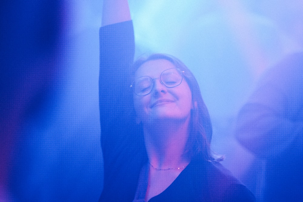 a woman with glasses is holding her arms up in the air