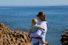 a woman holding a baby near the ocean
